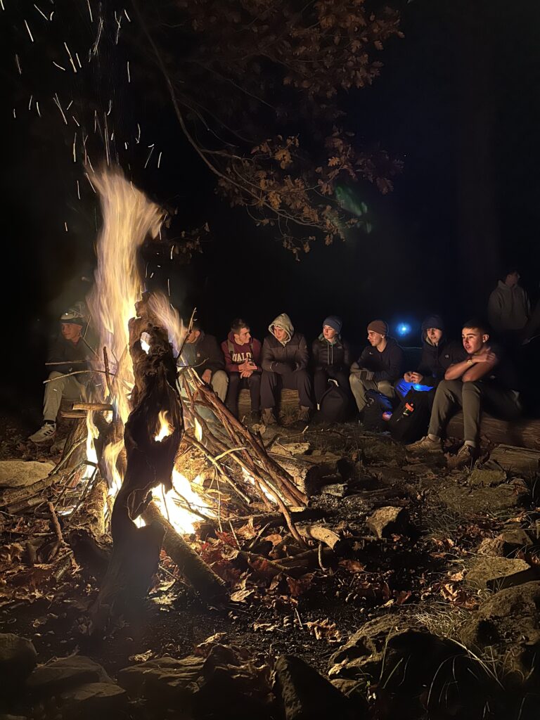 Midshipmen sit around a campfire at night